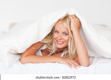 Smiling Woman Under A Duvet In Her Bedroom