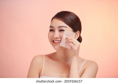 Smiling woman using facial oil blotting paper portrait.