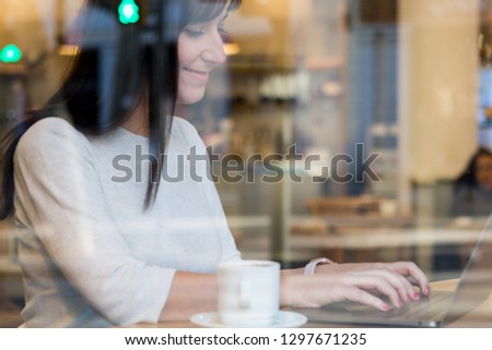 Smiling woman using laptop at cafe. Young beautiful girl sitting in a coffee shop and working on computer.