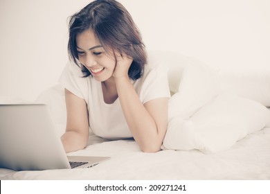 Smiling woman using a laptop while lying on her bed