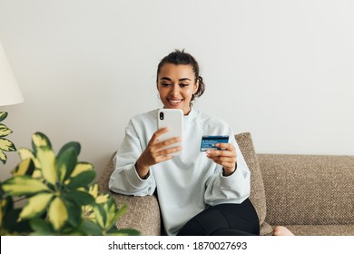 Smiling woman using smartphone and credit card. Young female making a purchase online.