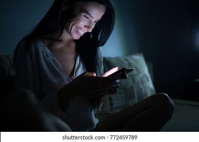 Smiling woman using smartphone at night dark room, online dating service