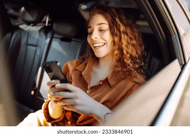 Smiling woman using smartphone while sitting in the back seat of a car. Young woman checks mail, texts, blogs in the car. Business, technology concept.