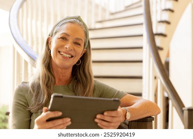 Smiling woman using tablet while sitting on staircase at home. Technology, digital, casual, lifestyle, connectivity, joy