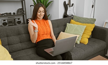 A smiling woman videoconferencing on a laptop in her modern living room with colorful cushions and a guitar in the background. - Powered by Shutterstock