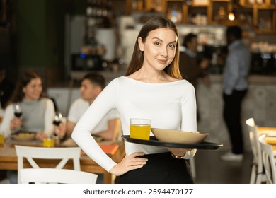 Sonriente mujer camarera sosteniendo una bandeja de comida delante del restaurante y Clientes. Camarera le invita a probar el plato del día en un restaurante europeo