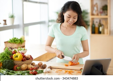 Smiling Woman Watching Tv Show On The Digital Tablet And Cooking Dinner