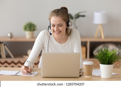 Smiling woman wear headset write notes watch webinar study work on laptop, young student in headphones learning computer course listening lecture training interpreter online teacher translating class