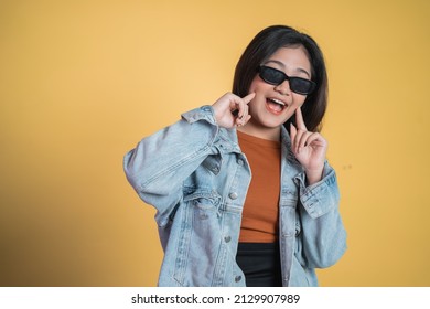 Smiling Woman Wear Sunglasses With Two Fingers Pointing To Cheek