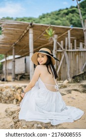 a smiling woman is wearing a backless white dress, sunbathing in the beach