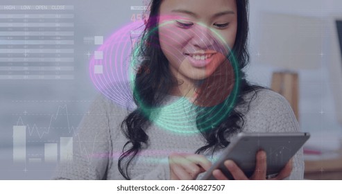 Smiling woman wearing grey sweater reviewing data on tablet at home office, with holographic charts. Technology, data, analytics, digital, professional, modern, workspace