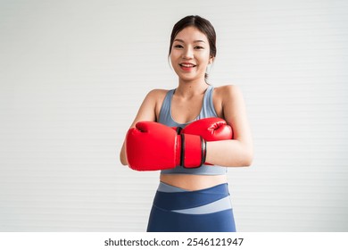 A smiling woman wearing red boxing gloves and athletic attire, ready to train, showcasing energy and confidence in a bright environment. - Powered by Shutterstock