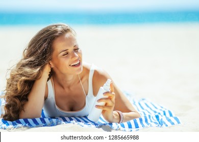 smiling woman in white beachwear with SPF laying on a striped towel on the ocean shore. sunscreen hight SPF with broad range UV UVB for maximum sunburn protection or hair protection conditioner.