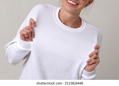 Smiling woman in white longsleeve holds his clothes with his hands, showing it. Text space. No face. Isolated on white
