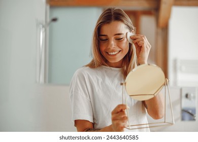 Smiling woman wiping her face with cotton pad in the bathroom. Skin care concept  - Powered by Shutterstock