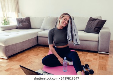 Smiling woman wiping off sweat with a towel after a home workout. Tired smiling woman relaxing on the floor after sports training. - Powered by Shutterstock