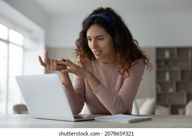 Smiling woman in wireless headphones chatting online with colleagues or business partners by video call, using laptop webcam, looking at screen, businesswoman teacher leading webinar, studying - Powered by Shutterstock