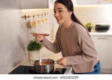 Smiling woman with wooden spoon tasting tomato soup in kitchen - Powered by Shutterstock