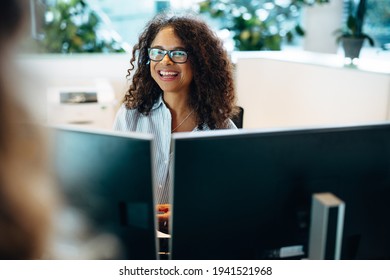 Smiling Woman Working At Front Desk Of A Municipality Office. Female Administrator Sitting Behind The Desk Looking At A Woman And Smiling.