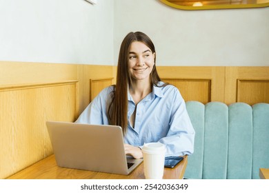 Smiling Woman Working on a Laptop in a Cozy Café Enjoying a Coffee During the Daytime - Powered by Shutterstock