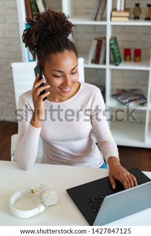 Smiling woman working on laptop in the office and talking on a smartphone . - Image