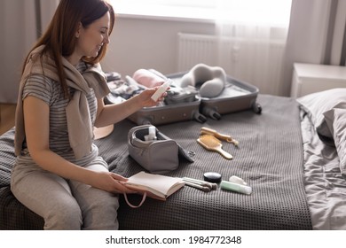 Smiling woman writing list of necessary cosmetics getting ready to trip vacation. Happy female making notes in notebook of hygienic, cleanser, make up and washing remedy. Comfy storage organization