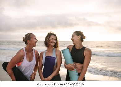 Smiling women at the beach talking to each other holding yoga mats. Fitness women standing at the sea shore to do yoga. - Powered by Shutterstock