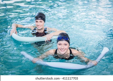 Smiling women in the pool with foam rollers at the leisure center