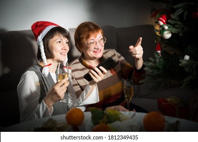 Smiling Women Watching Christmas Tv Program Sitting At Table With Wine Glasses In Dark Room