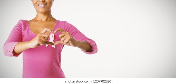 Smiling Women Wearing Pink Shirt Making Heart With Their Fingers Around Pink Ribbon On A White Background