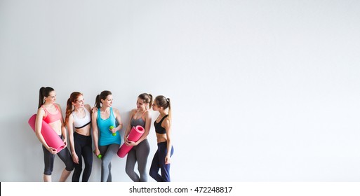 Smiling women yoga / fitness class. Young athletic women friends with yoga mats and dumbbells on a white background.