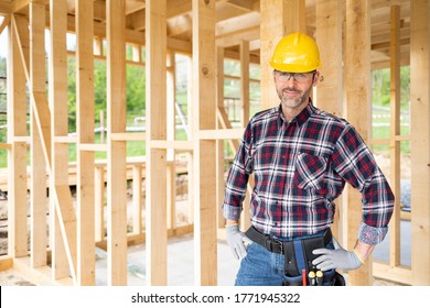 Smiling worker on building site with frame house construction in background - Shutterstock ID 1771945322