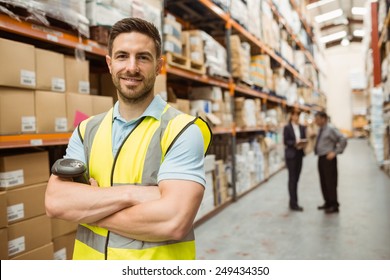 Smiling worker standing with arms crossed in a large warehouse - Powered by Shutterstock