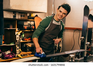 Smiling Worker Waxing Ski With Wax Iron In Repair Shop