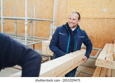 Smiling worker in a woodworking factory or warehouse collecting a large wooden beam off the storage racks with a colleague