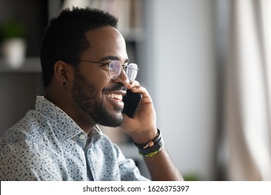 Smiling young adult african american hipster business man professional making business call talking on the phone in office enjoying corporate mobile conversation indoors, closeup side profile view