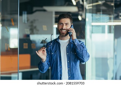 Smiling Young Adult Bearded Hipster Professional Business Man Making A Business Call While Talking On The Phone In The Office, Enjoying A Corporate Mobile Conversation Indoors, Close Up