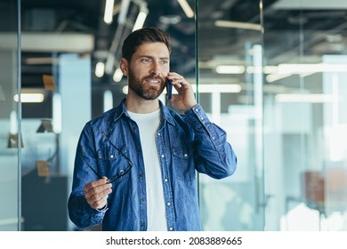 Smiling Young Adult Bearded Hipster Professional Business Man Making A Business Call While Talking On The Phone In The Office, Enjoying A Corporate Mobile Conversation Indoors, Close Up