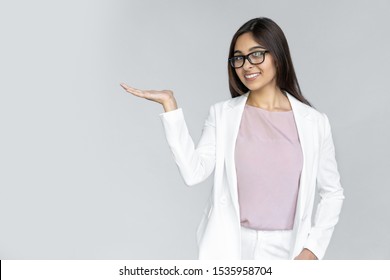 Smiling young adult indian businesswoman in formal wear suit holding invisible object copy space on open palm hand. Happy  woman looking at camera standing isolated on grey background with copy space - Powered by Shutterstock