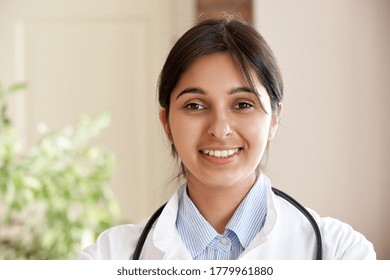 Smiling Young Adult Indian Female Doctor Gp Wear White Coat Looking At Camera In Medical Clinic Office. Happy Beautiful Health Care India Professional Medic Physician, Therapist, Gp Headshot Portrait.