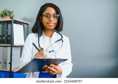 Smiling Young Adult Indian Female Doctor Wear White Coat In Medical Clinic Office. Happy Beautiful Health Care India Professional Medic Physician, Therapist, Headshot Portrait.