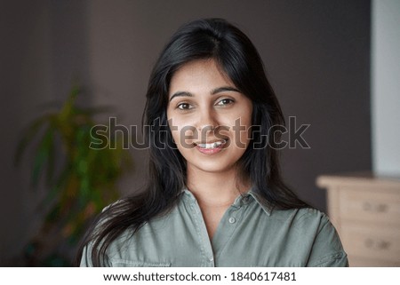 Smiling young adult indian woman looking at camera at home or in office. Pretty lady standing in India house apartment, teacher, real estate agent, housewife close up face front headshot portrait.