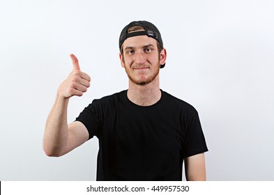 Smiling Young Adult Male In Dark T-Shirt And Baseball Hat Worn Backwards Shows His Thumbs Up