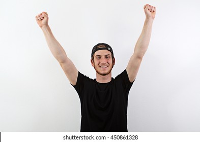 Smiling Young Adult Male In Dark T-Shirt And Baseball Hat Worn Backwards With Arms Raised