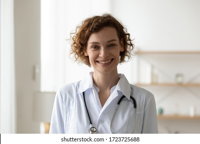 Smiling young adult woman doctor wearing white medical coat and stethoscope head shot close up portrait. Happy female physician, therapist, general practitioner looking at camera standing in hospital.