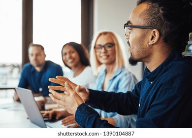 Smiling young African American businessman discussing work with a diverse group of colleagues sitting together at an office table
