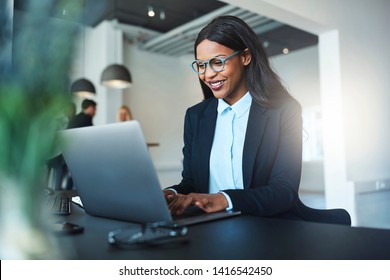 Smiling young African American businesswoman working online with a laptop while sitting at her desk in a bright modern office