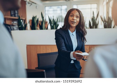 Smiling young African American concierge helping two guests check in while working behind a hotel reception counter - Powered by Shutterstock