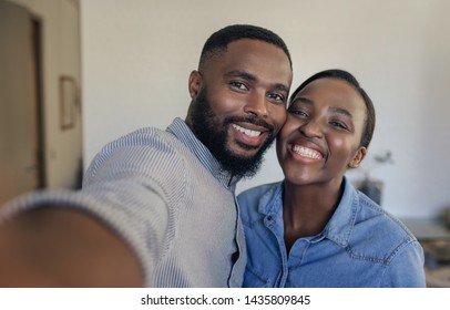 Smiling young African American couple standing in their living room at home taking selfies together - Shutterstock ID 1435809845
