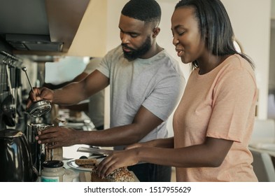 Smiling Young African American Couple Standing At Their Kitchen Counter In The Morning Preparing Breakfast And Making Coffee Together